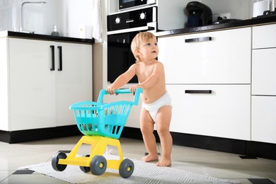 Photo of Cute baby making first steps with toy walker in kitchen. Learning to walk