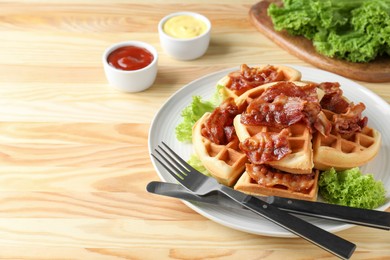 Photo of Tasty Belgian waffles served with bacon, lettuce and sauces on wooden table. Space for text