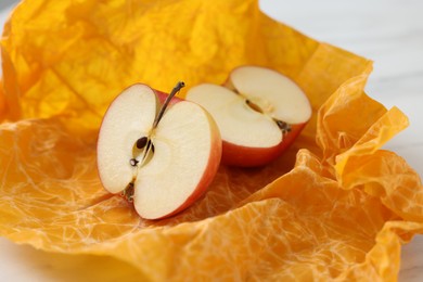 Photo of Halves of apple with orange beeswax food wrap on table, closeup