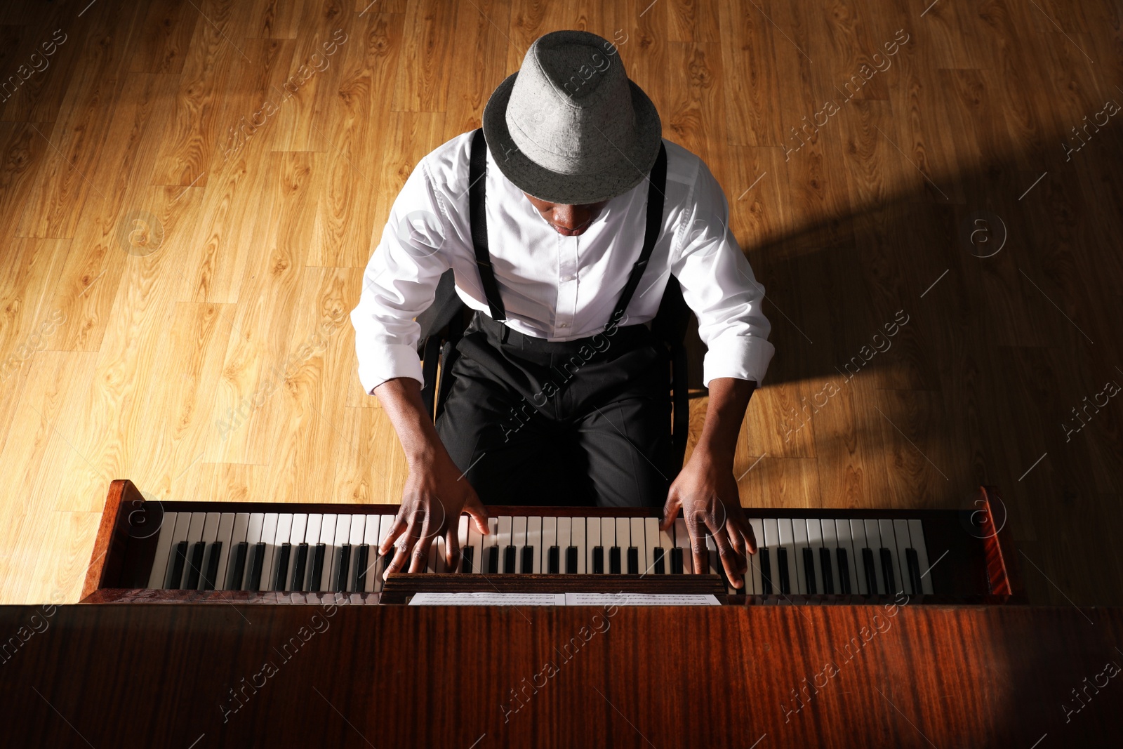 Photo of African-American man playing piano indoors, above view. Talented musician