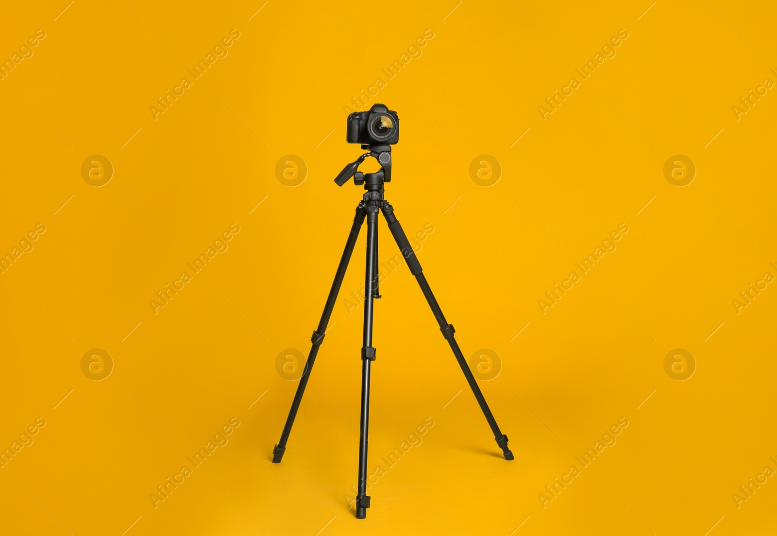 Photo of Modern tripod with professional camera on yellow background