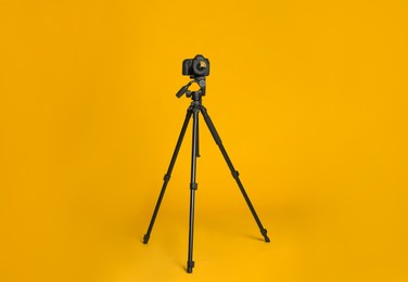 Modern tripod with professional camera on yellow background