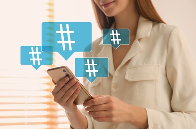 Image of Woman using modern smartphone indoors, closeup. Hashtag symbols over device