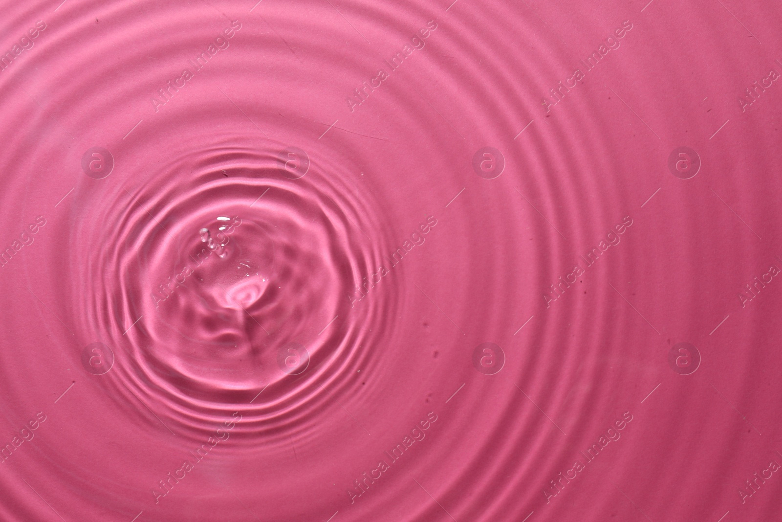 Photo of Rippled surface of clear water on bright pink background, top view