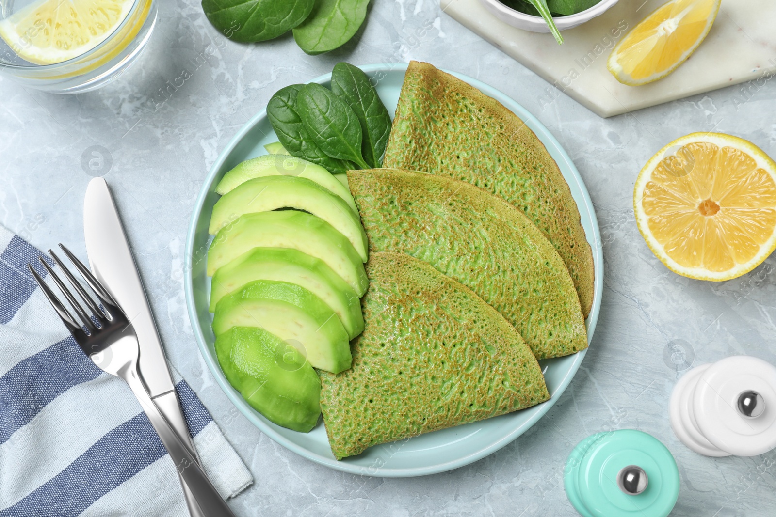 Photo of Delicious spinach crepes with avocado served on marble table, flat lay