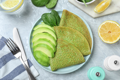 Delicious spinach crepes with avocado served on marble table, flat lay