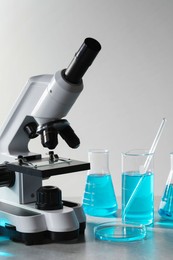 Photo of Different laboratory glassware with light blue liquid and microscope on table