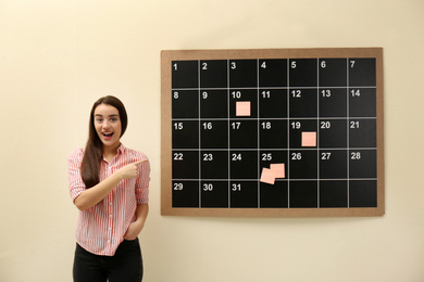 Photo of Young beautiful woman near board calendar  indoors