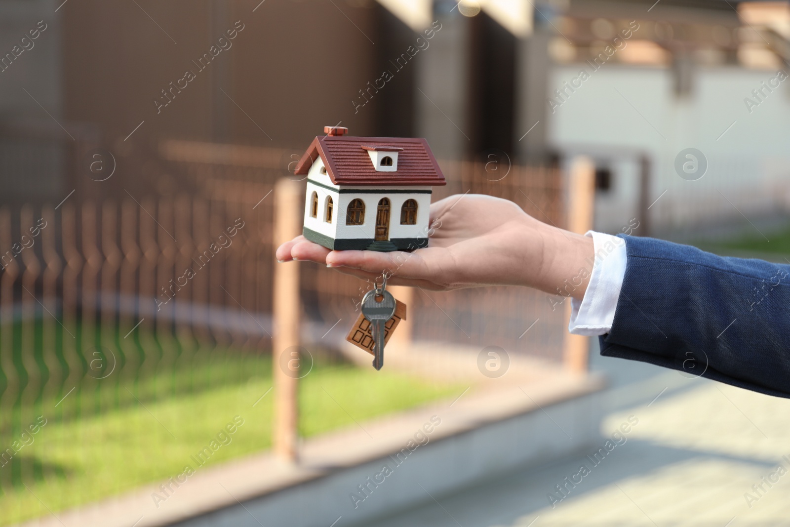 Photo of Real estate agent holding key and house model outdoors, closeup