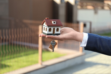 Photo of Real estate agent holding key and house model outdoors, closeup