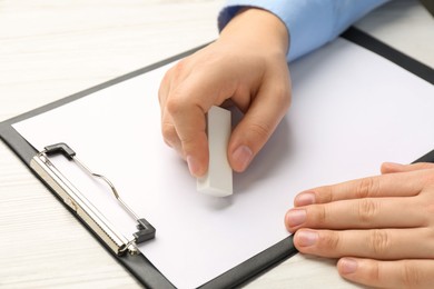 Photo of Man erasing something on paper at white wooden table, closeup