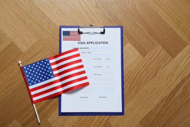 Photo of Visa application form for immigration and small American flag on table, flat lay