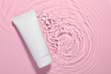Photo of Tube of facial cleanser in water against pink background, top view. Space for text