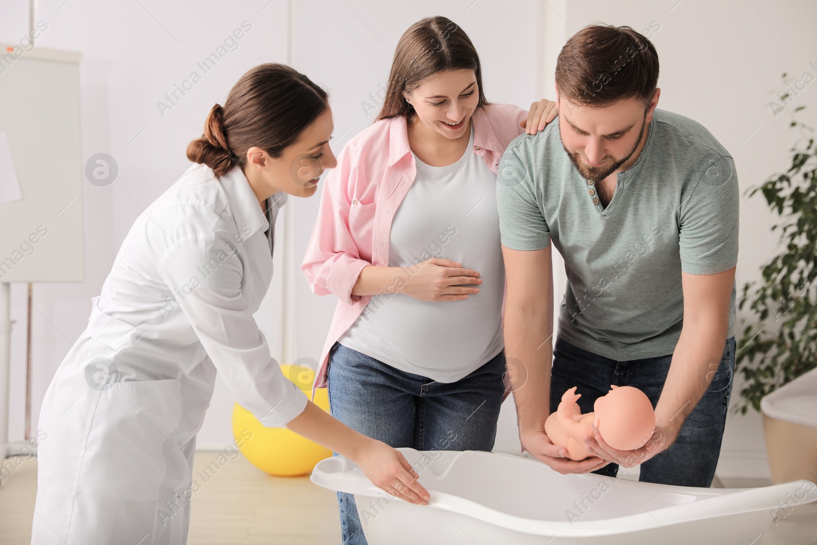 Photo of Man with pregnant wife learning how to bathe baby at courses for expectant parents indoors