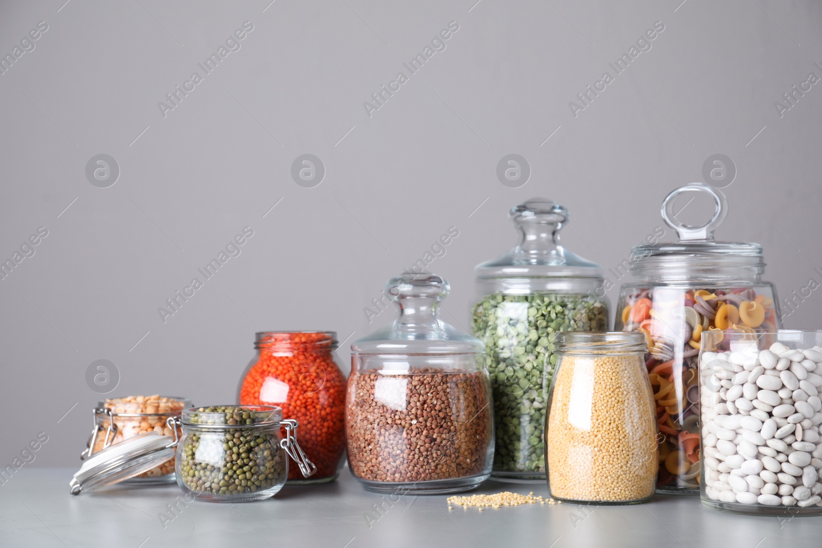 Photo of Jars with different cereals on grey table