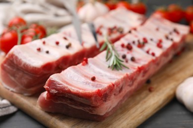 Photo of Raw pork ribs with peppercorns and rosemary on table, closeup