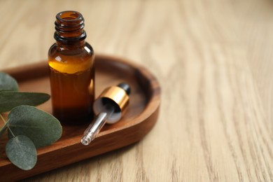 Aromatherapy. Bottle of essential oil and eucalyptus leaves on wooden table, closeup. Space for text