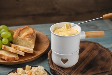 Pot of tasty cheese fondue and fork with bread on blue wooden table