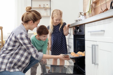 Mother and her children taking out cookies from oven in kitchen