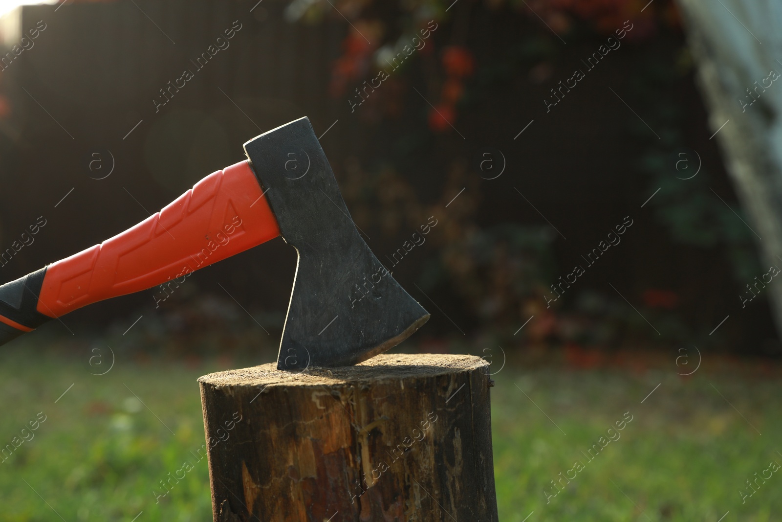Photo of Metal axe in wooden log on backyard, closeup