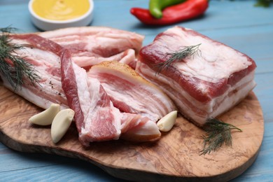 Pieces of pork fatback with garlic and dill on light blue wooden table, closeup