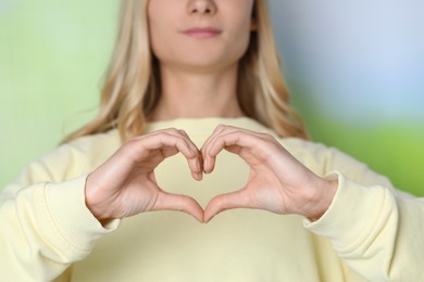 Woman making heart with hands on blurred background, closeup