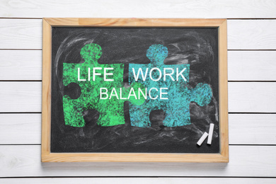 Image of Work-life balance concept. Chalkboard with drawing of connected puzzle pieces on wooden background, top view