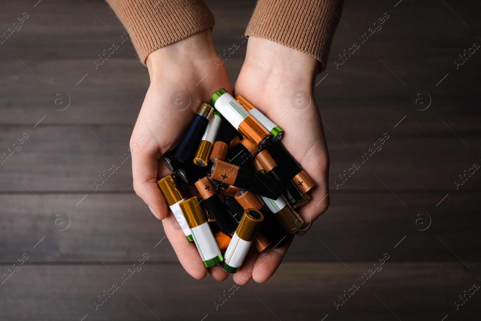 Image of Woman holding many used electric batteries in her hands over wooden table, closeup