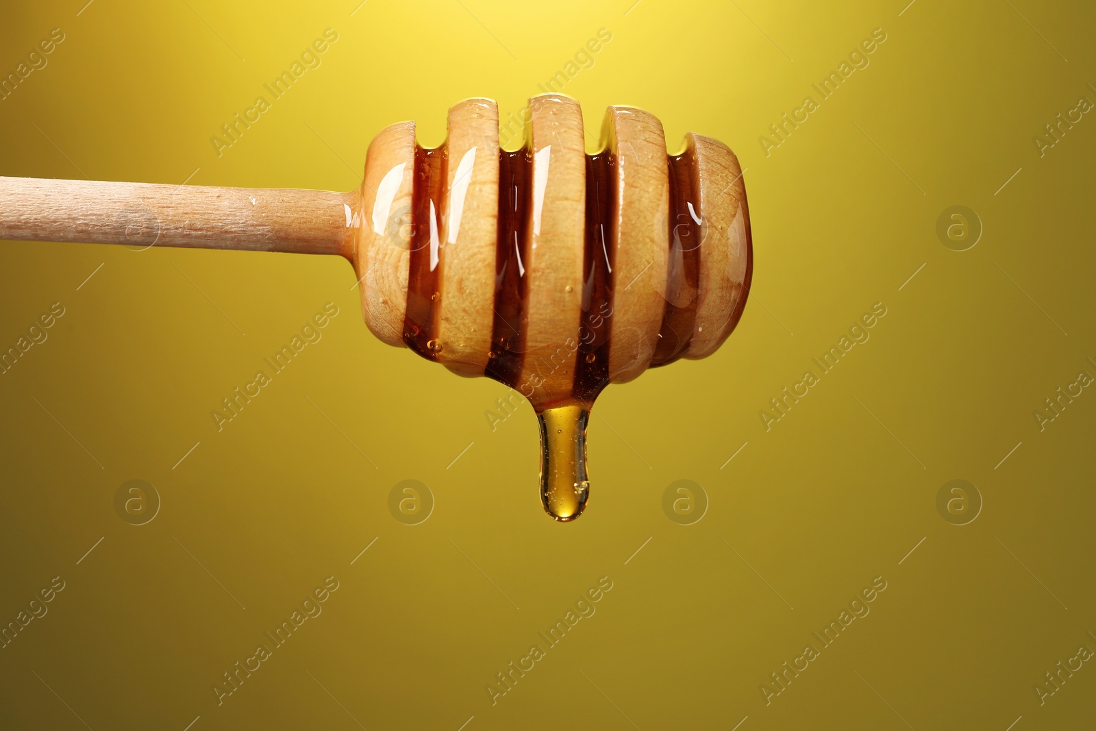 Photo of Delicious honey flowing down from dipper against golden background, closeup. Space for text