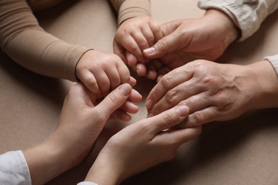 Photo of Family holding hands together on brown background, closeup