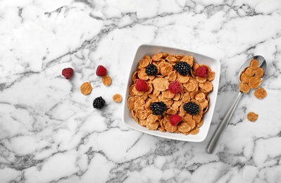 Photo of Bowl with cornflakes and berries on marble table, top view. Whole grain cereal for breakfast