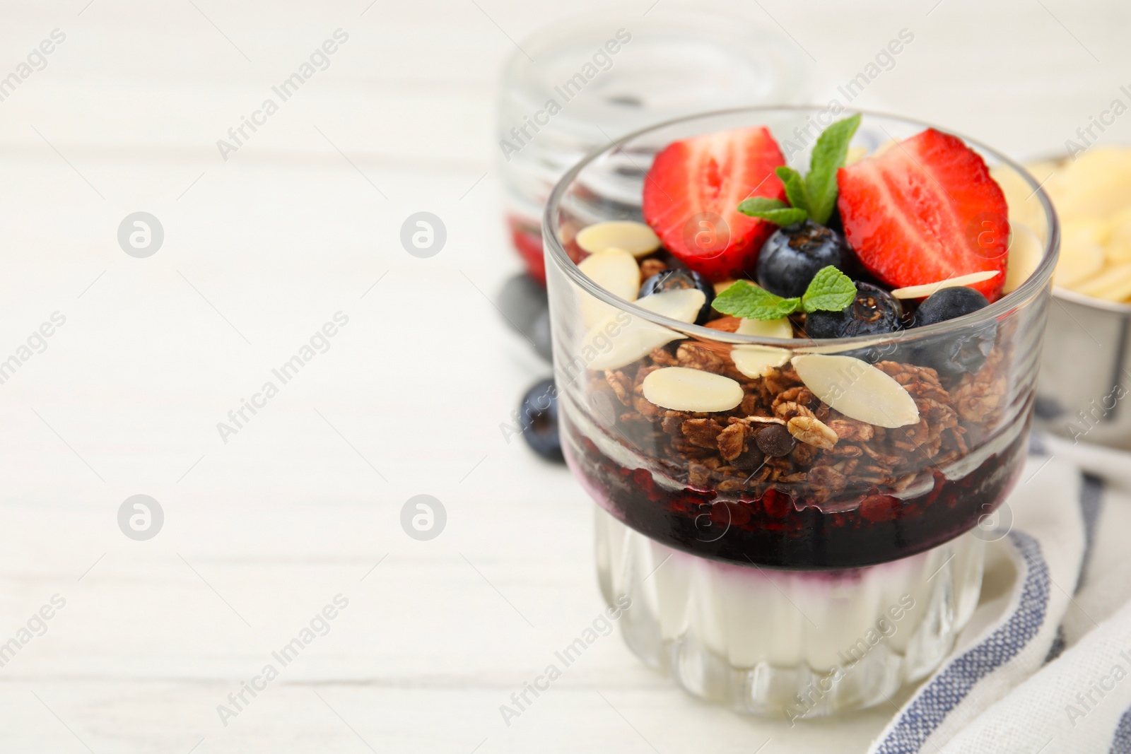 Photo of Tasty granola with berries, jam, yogurt and almond flakes in glass on white table, closeup. Space for text