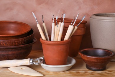 Set of different crafting tools and clay dishes on wooden table in workshop