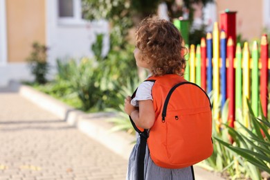 Photo of Little girl walking to kindergarten outdoors on sunny day, back view. Space for text