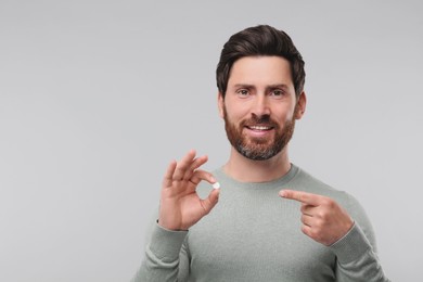 Handsome man with pill on light grey background, space for text