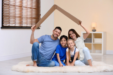 Happy family sitting under cardboard roof at home. Insurance concept