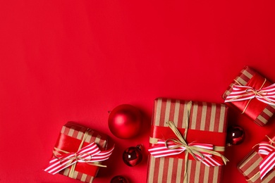 Photo of Gift boxes with Christmas balls on bright red background, flat lay. Space for text