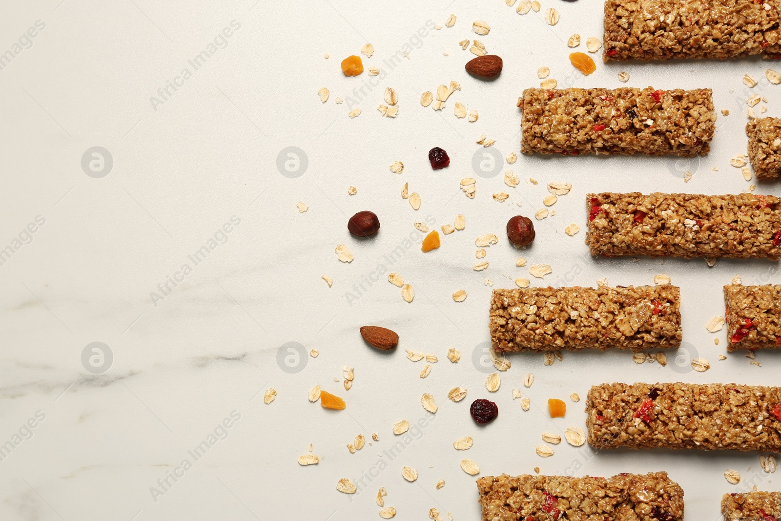 Photo of Tasty granola bars and ingredients on white marble table, flat lay. Space for text