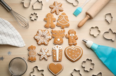 Photo of Christmas tree shape made of delicious gingerbread cookies surrounded by kitchen utensils on wooden table, flat lay