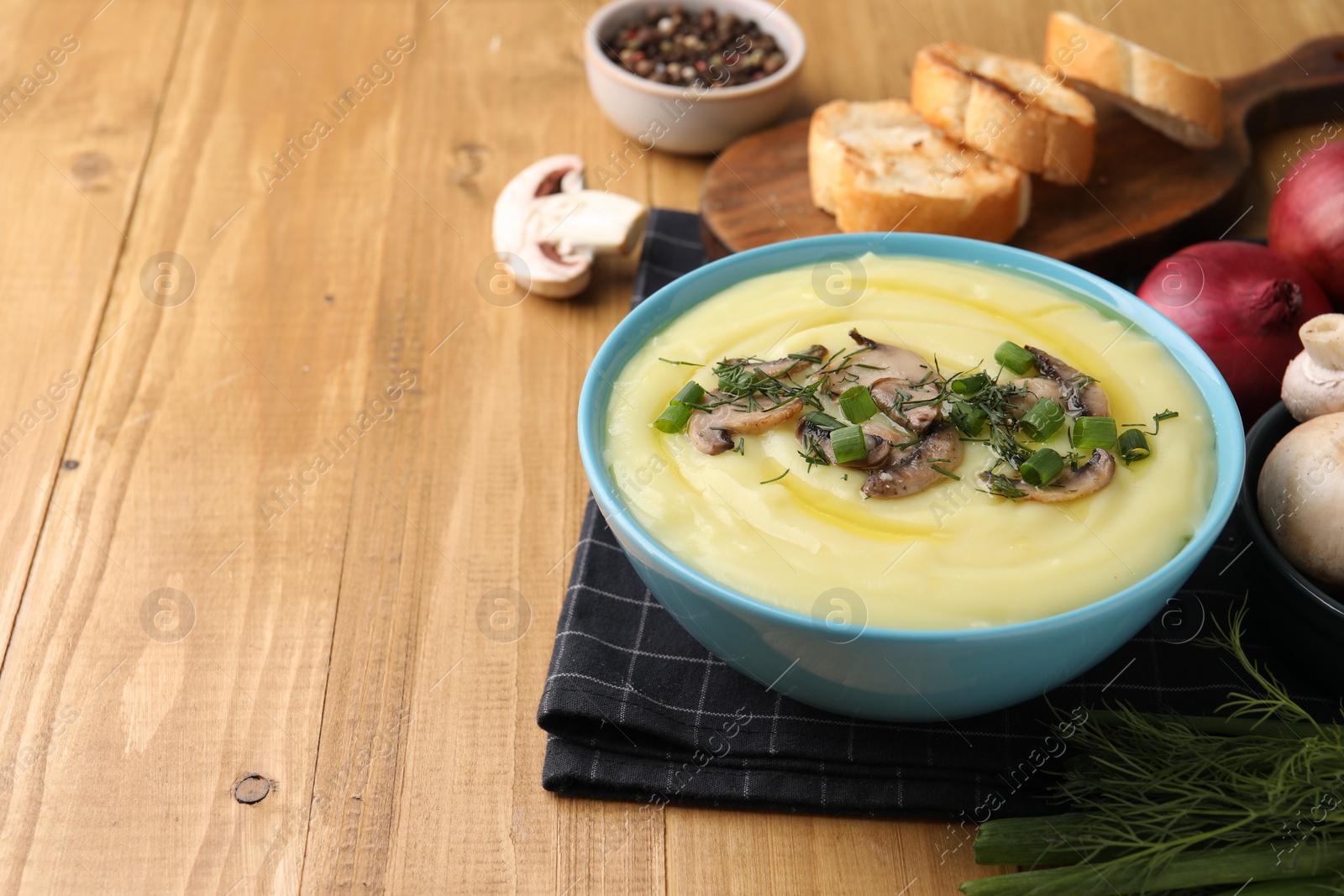 Photo of Bowl of tasty cream soup with mushrooms, green onions and dill on wooden table. Space for text