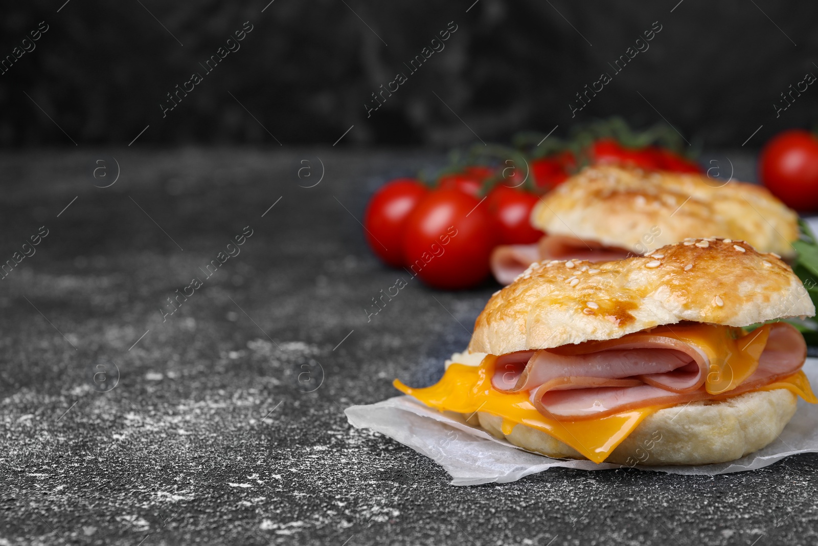 Delicious bagels with ham and cheese on dark grey textured table, space for text Photo of Delicious bagels with ham and cheese on dark grey textured table, space for text