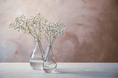 Photo of Gypsophila flowers in vases on table against brown background. Space for text
