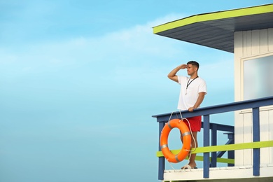 Photo of Male lifeguard on watch tower against blue sky