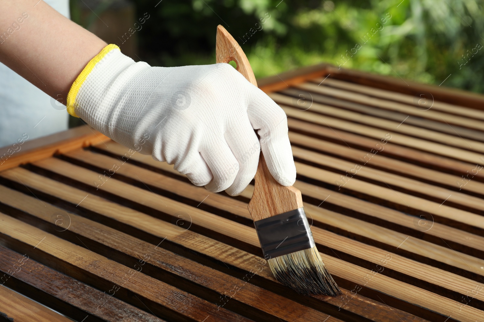 Photo of Woman applying wood stain onto planks outdoors, closeup