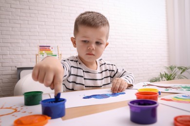 Photo of Little boy painting with finger at wooden table in room