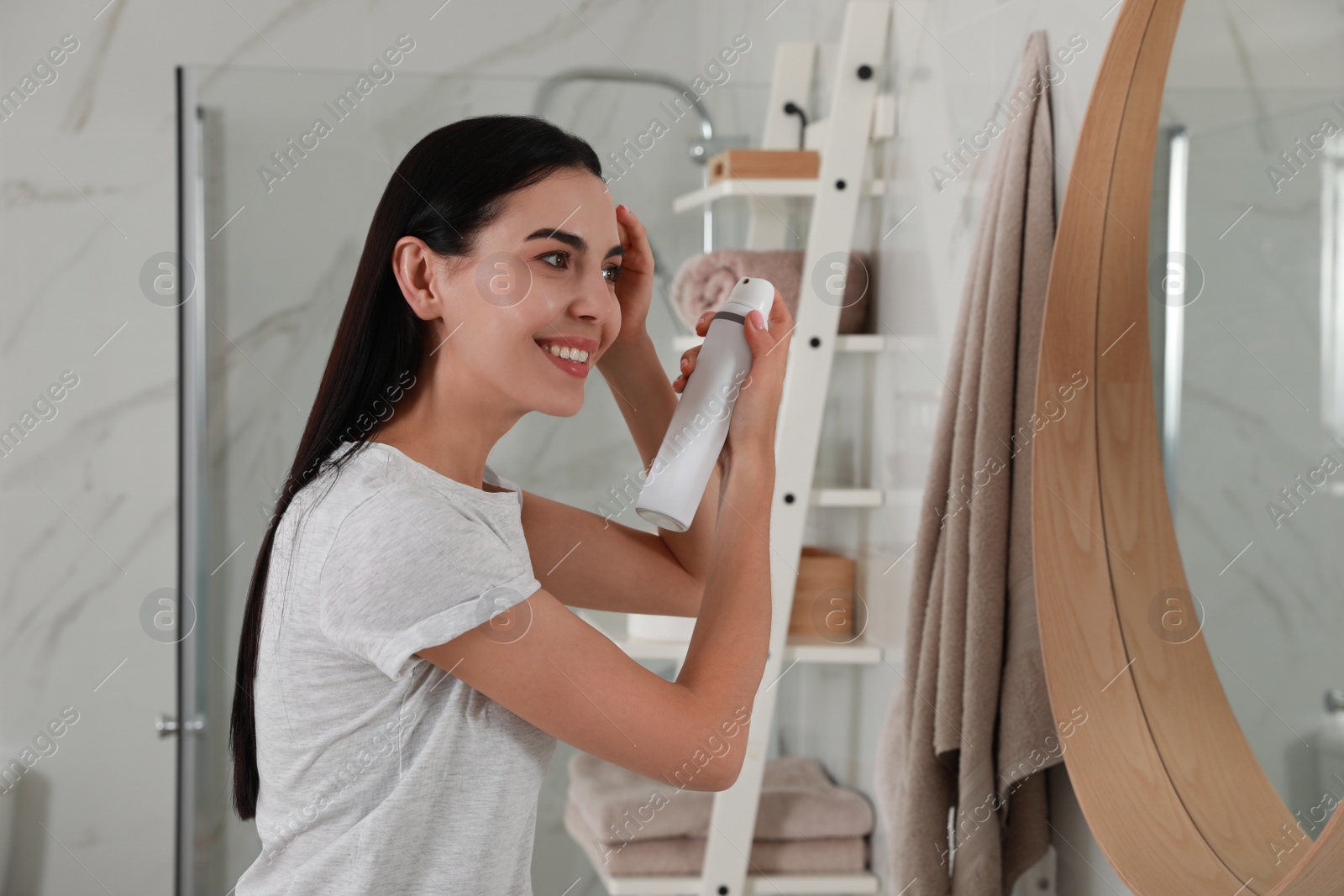 Photo of Woman applying dry shampoo onto her hair near mirror in bathroom