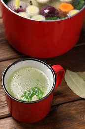 Red mug with tasty bouillon on wooden table