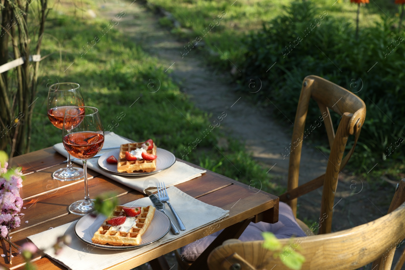 Photo of Delicious Belgian waffles with fresh strawberries and wine served on table in spring garden