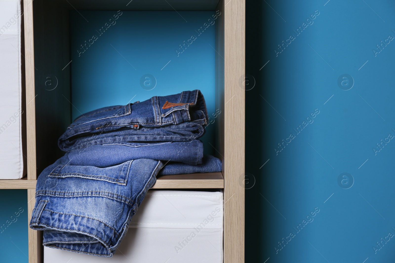 Photo of Stack of different jeans in wardrobe against color wall with space for text