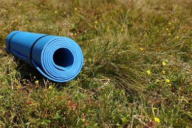 Rolled blue soft sleeping pad on grass, space for text